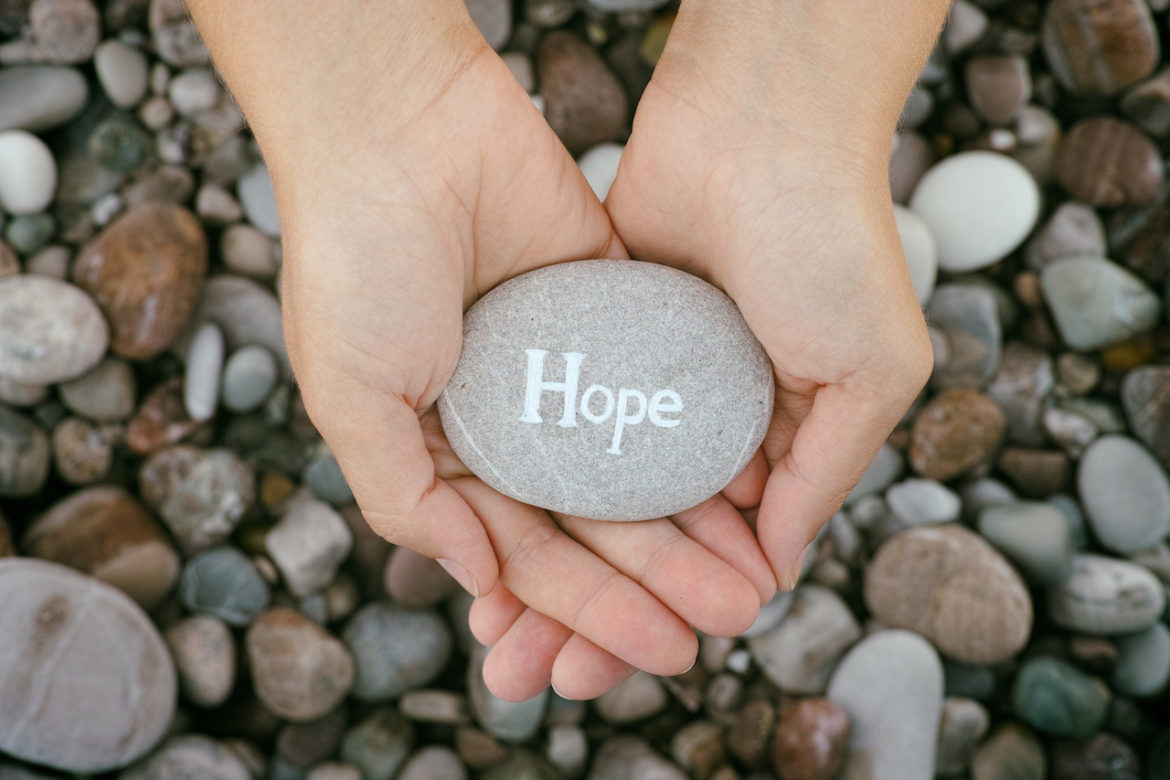 close up of woman holding in palm of her hands a stone with engraved word hope