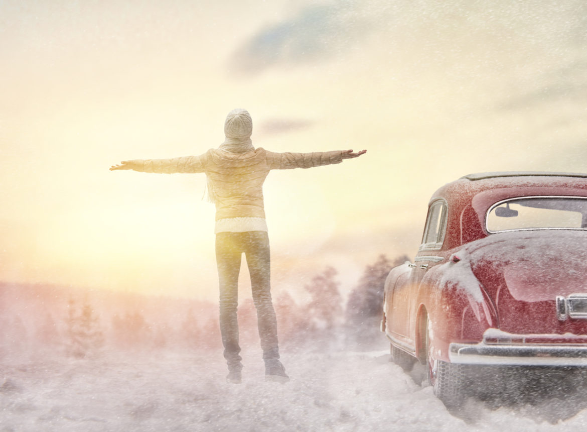 woman at peace during road trip standing with arms outstretched by red car in spring wintery weather