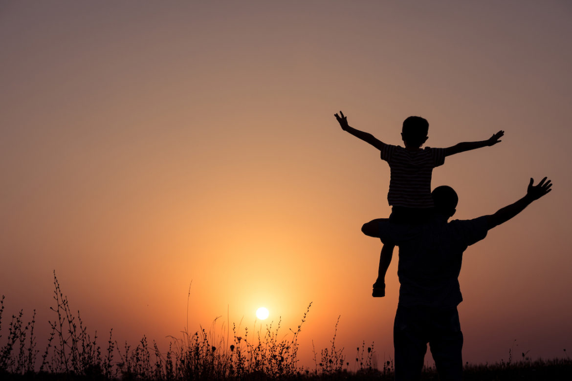 better life son on father's shoulder with both arms reaching out enjoying a beautiful sunset together