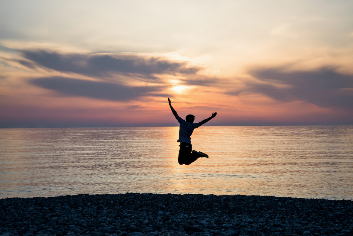 happy male silhouette at sunrise on a beach jumping high with arms outstretched