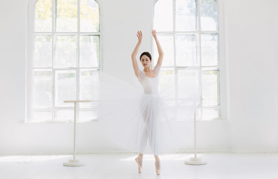 ballerina dressed in white dancing solo in a white studio infused with light