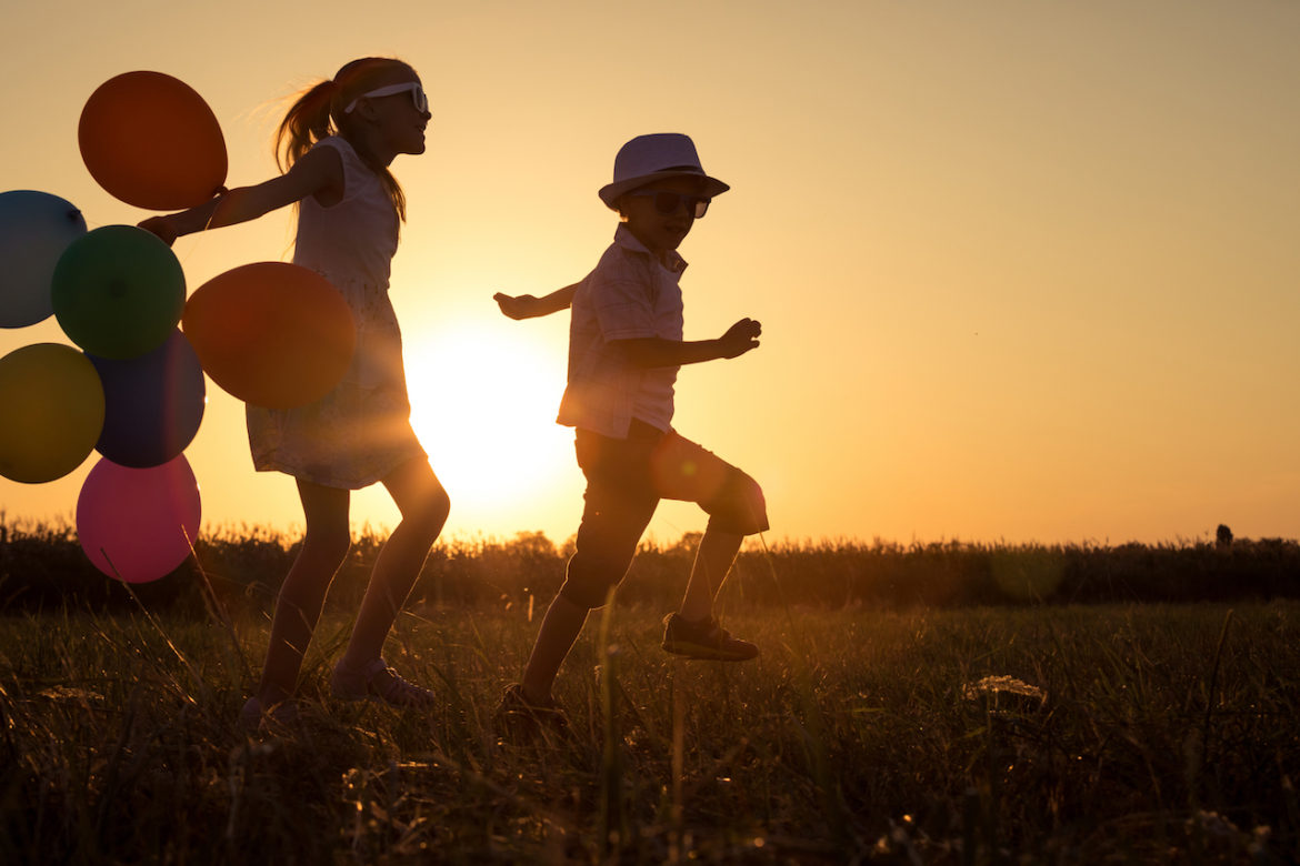 flower child silhouette of happy siblings playing with balloons on a field at sunset