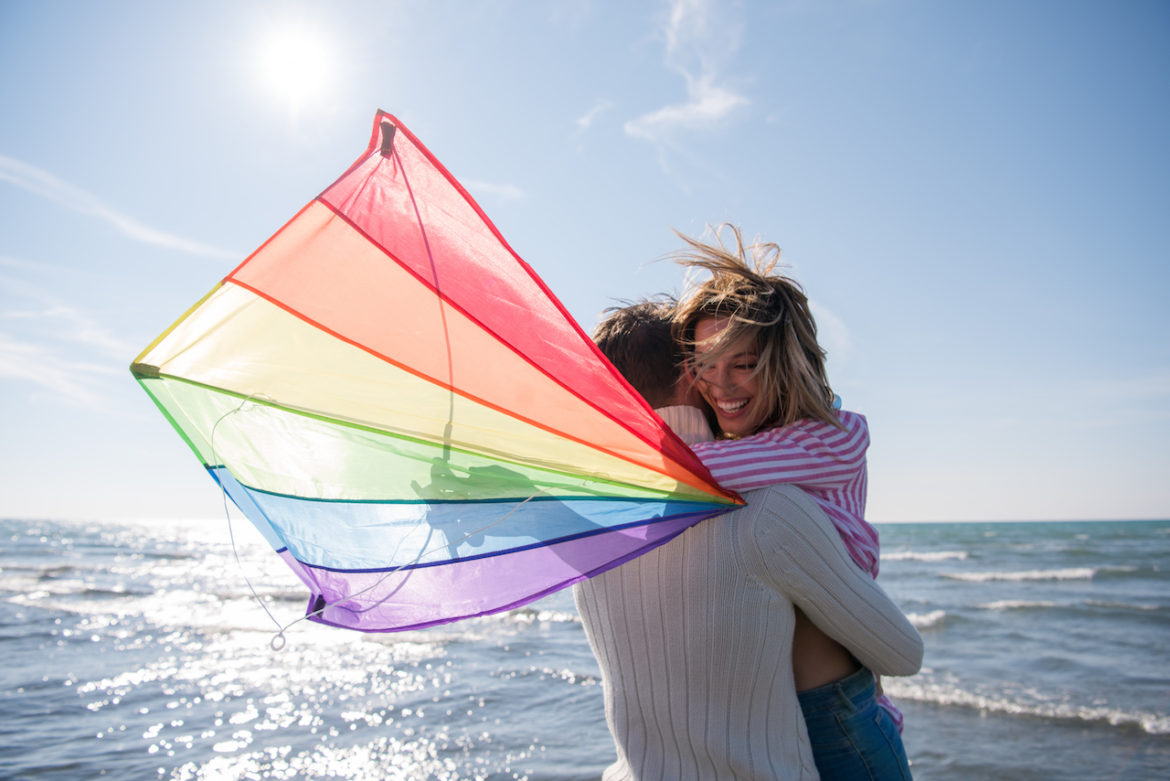 couple enjoy meaningful time together in an embrace holding a colorful kite at the beach on autumn day