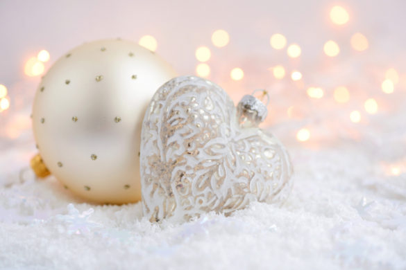 Joy of remembering two Christmas ornaments on snow with Christmas lights in background.