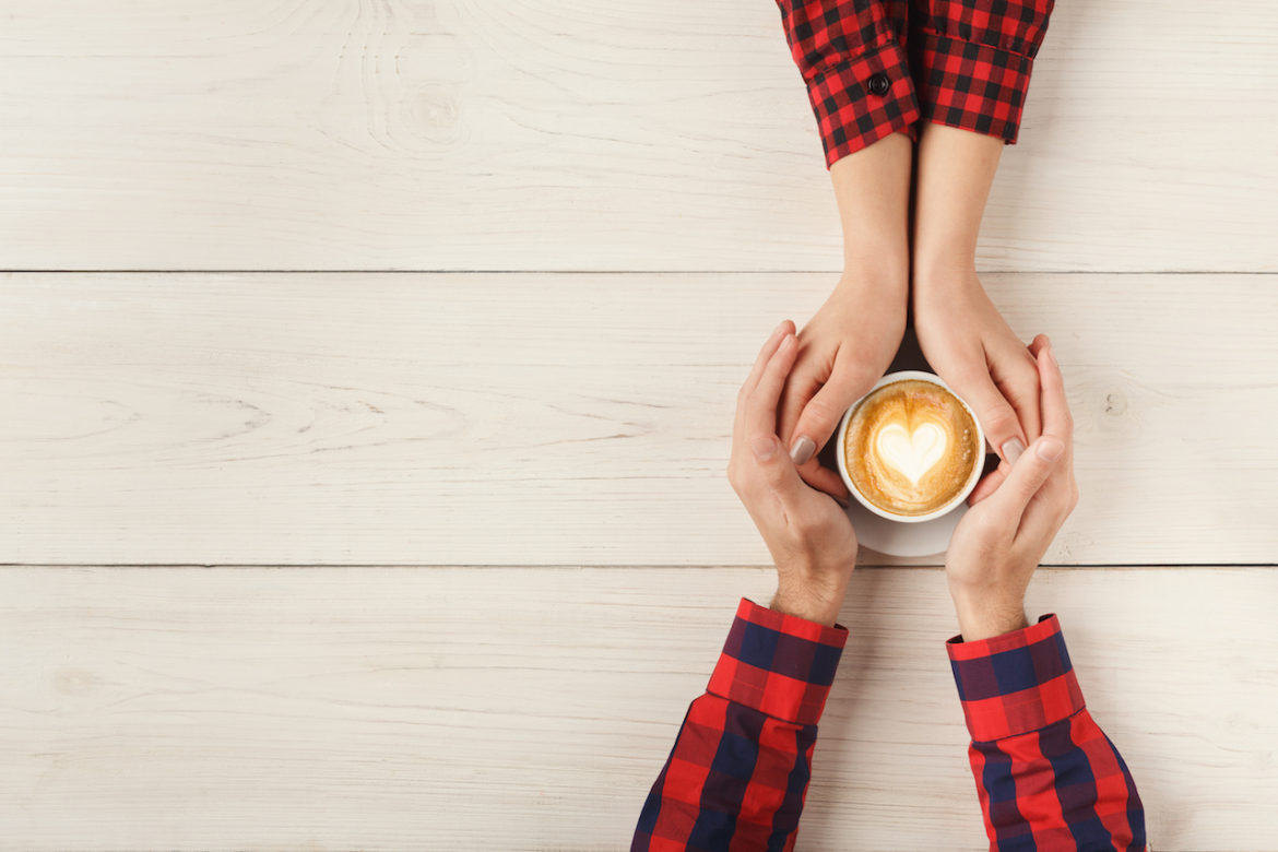 table top view of couple in love with cupped hands around latte with heart in center