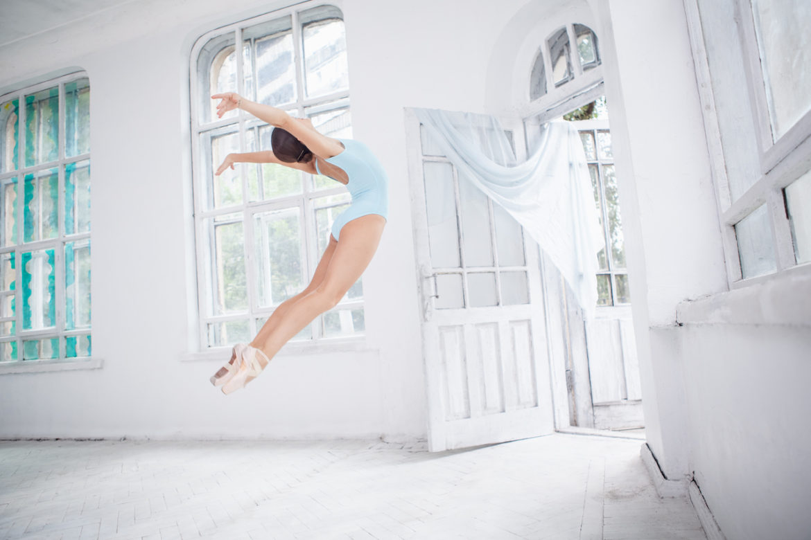 power and freedom expressed as young modern ballet dancer jumps with joy in whitewashed studio with large french paned windows