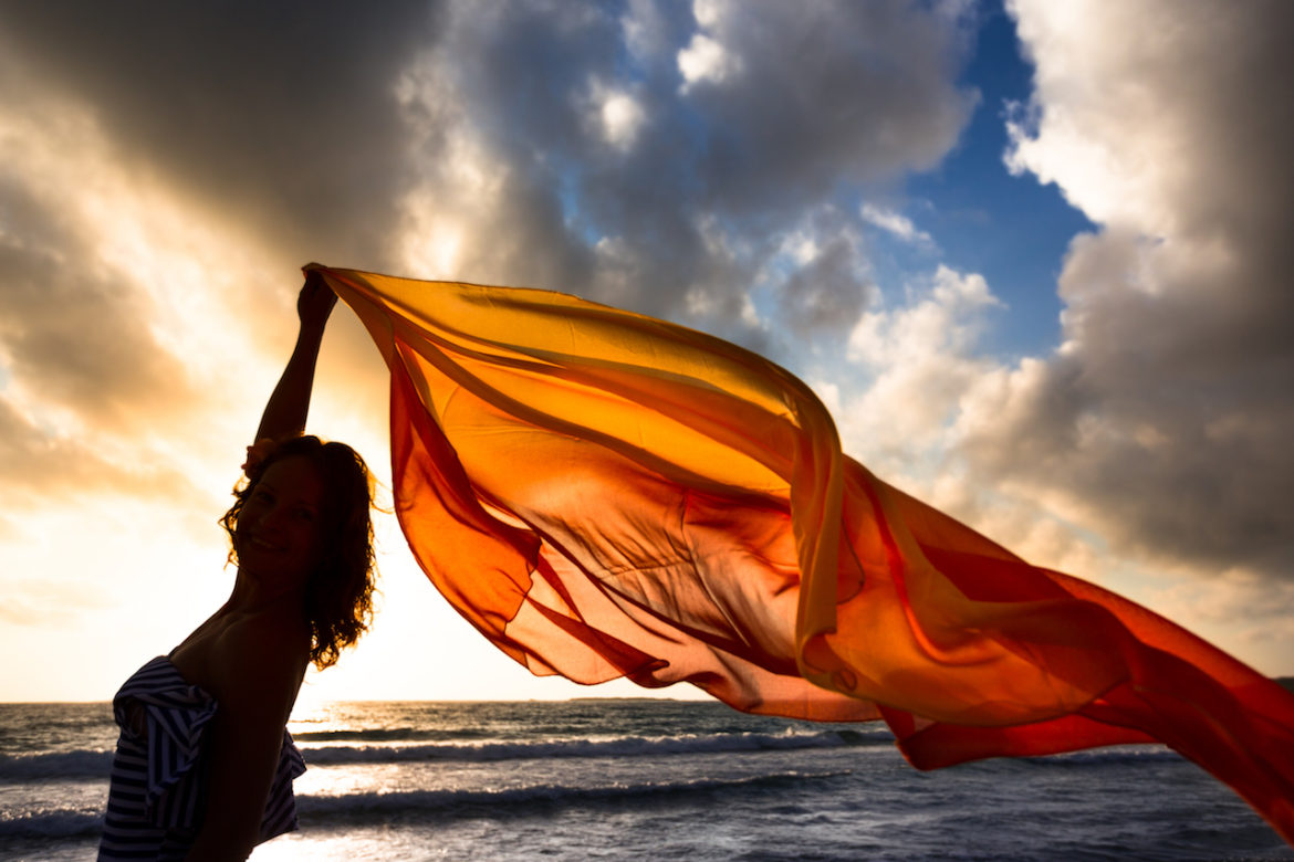 silhouette of a woman holding up a red silk scarf on a windy day at the beach knowing the war within when without love.