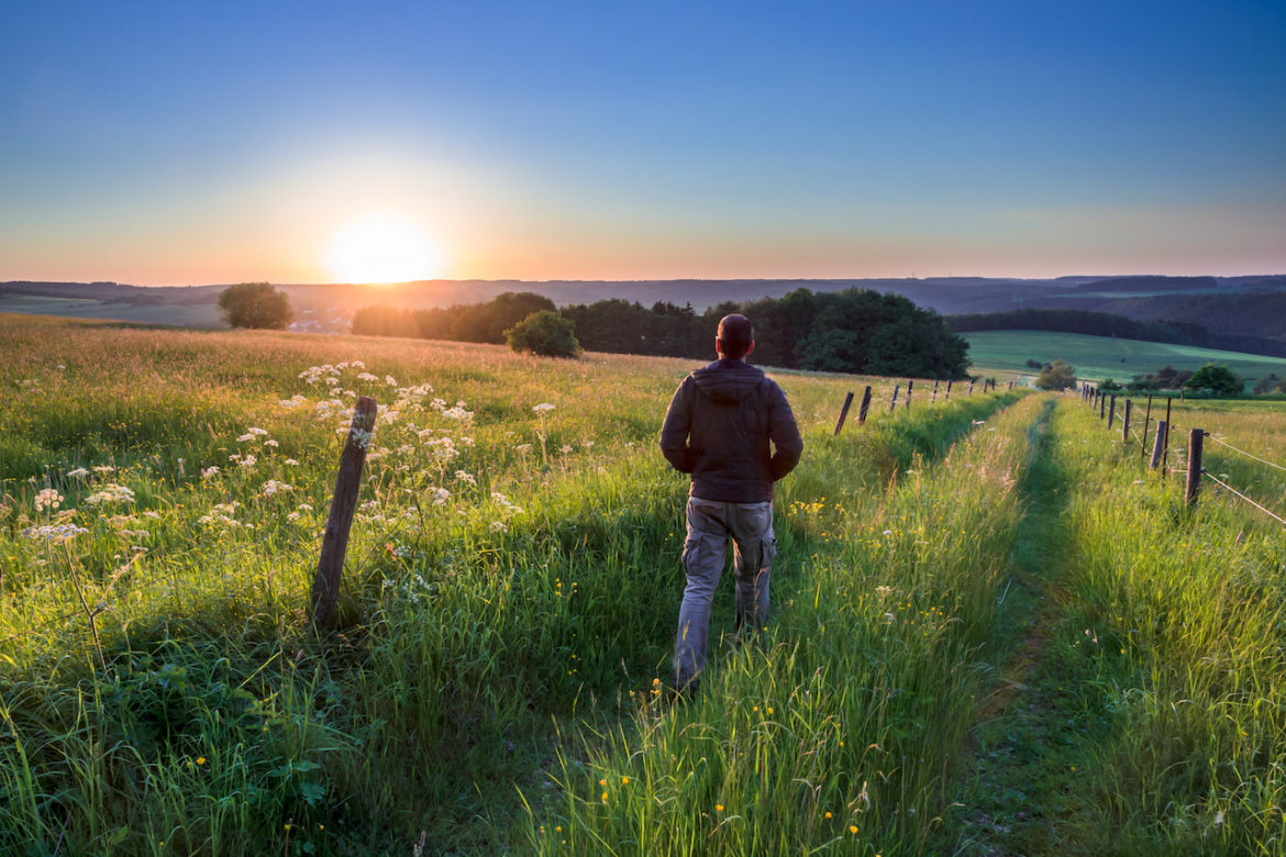 a man knows the secret to a great life as he walks on a prairie field facing the sunset.