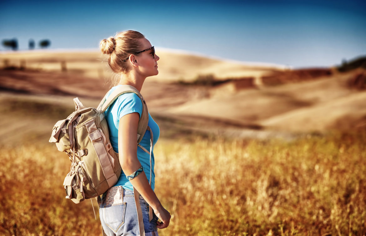 Outside the comfort zone, female tourist enjoying view of dry golden wheat hills, traveling through Europe early autumn.