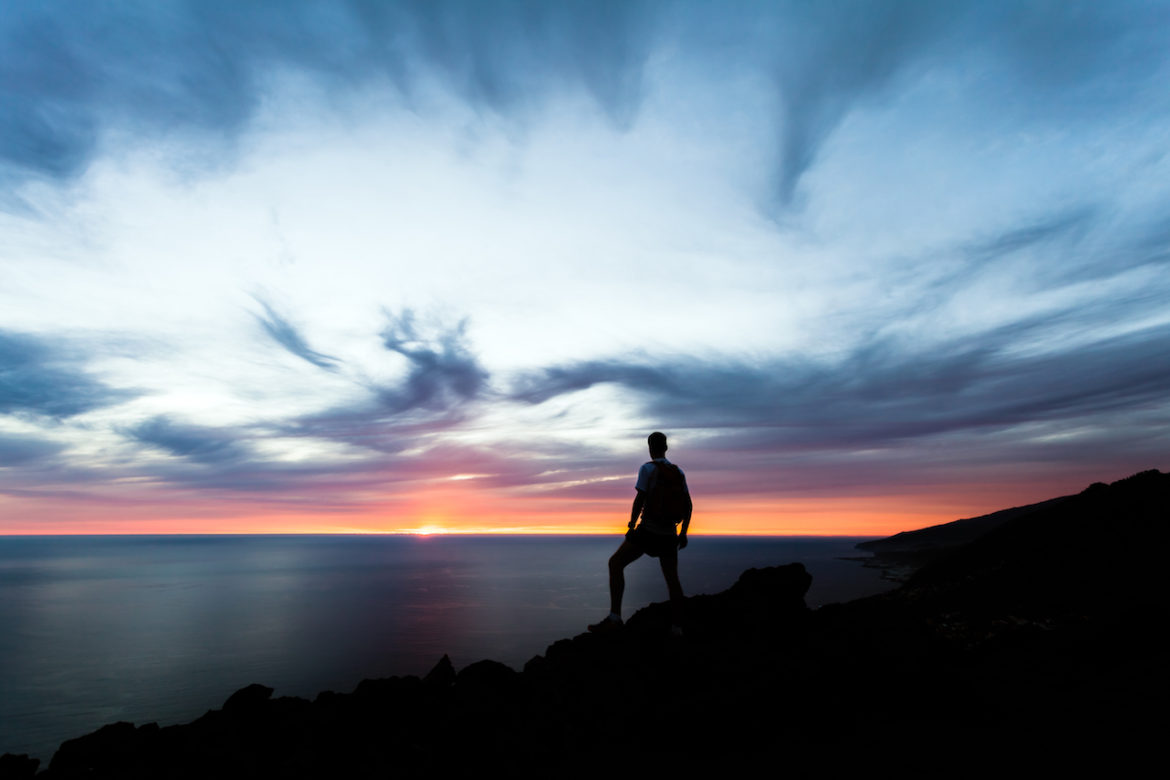 male hiker takes me time admiring sunset on top of a mountain overlooking the ocean