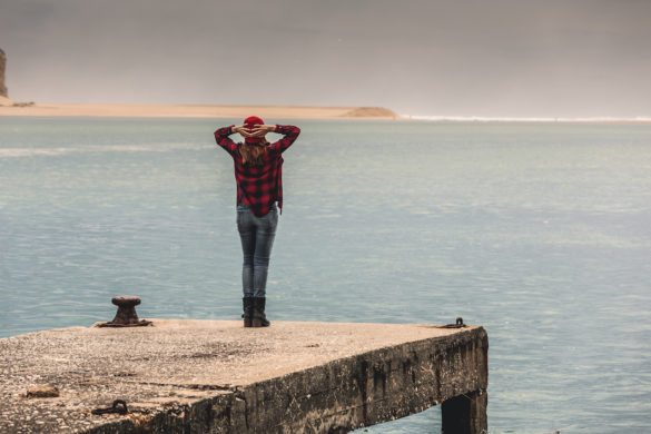 woman at the lake in fall standing on a pier arms raised and hands behind her head loving her freedom after forgiveness