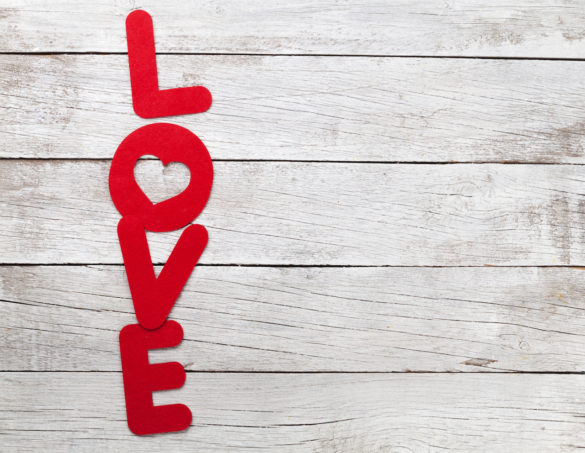 the power of unconditional love in the word of love spelled out in red vertically placed over a white washed wooden backdrop