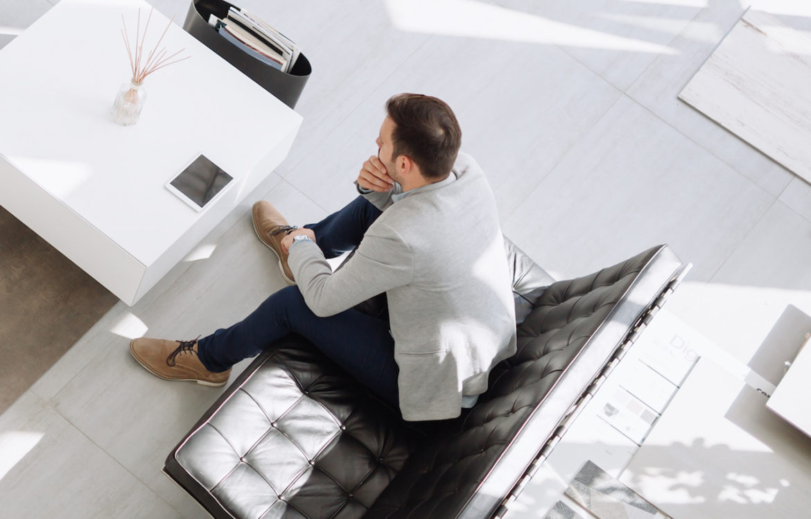 following an ultimatum well dressed business man must decide while seated in a brightly lit modern staff room with hand on chin