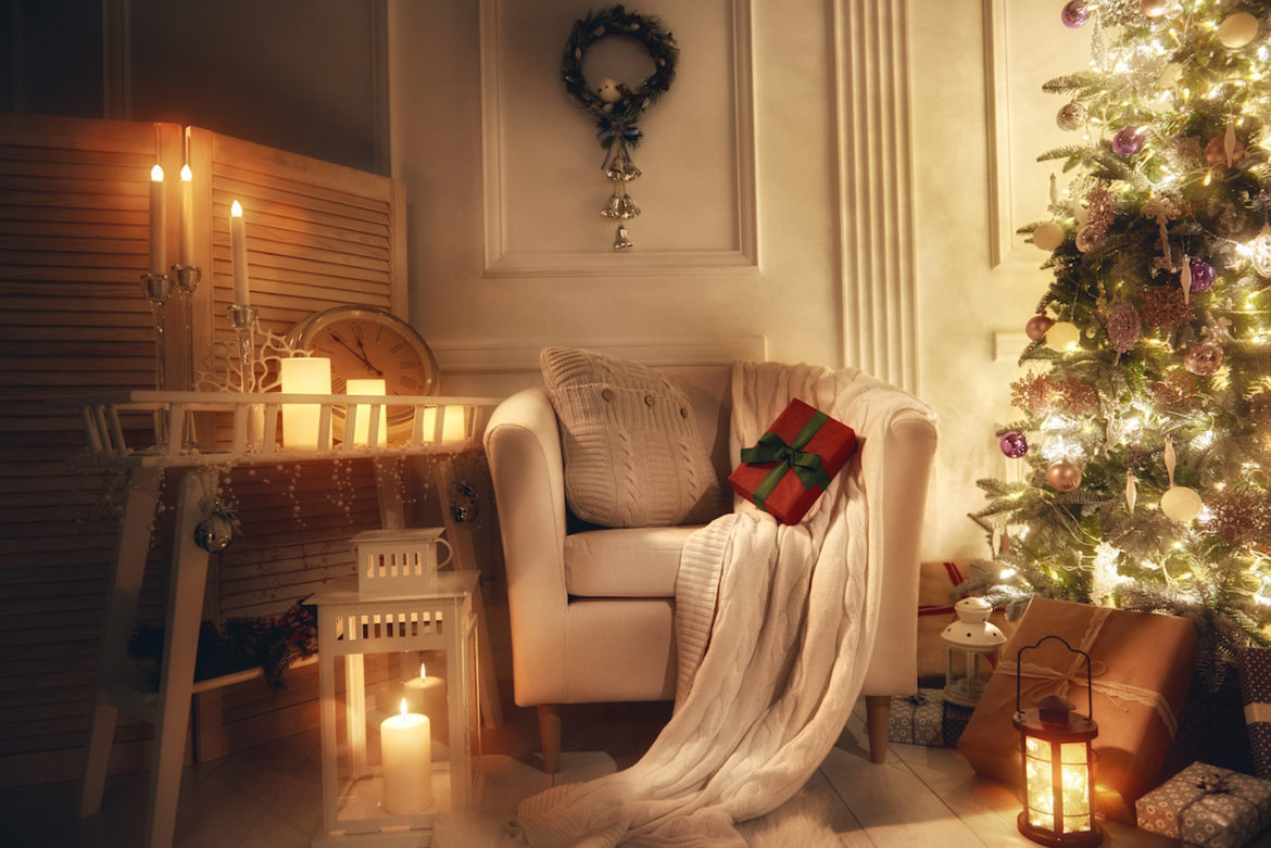 a favorite corner decorated for comfort with lit candles a comfy chair an afghan a cushion and a Christmas tree
