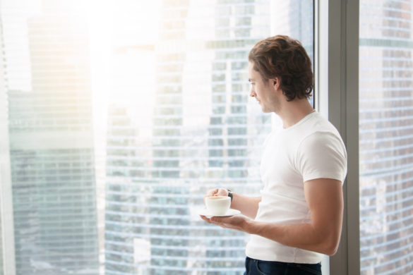 man near wall of windows enjoying a cup of coffee while looking out from office knowing if given half a chance he will succeed