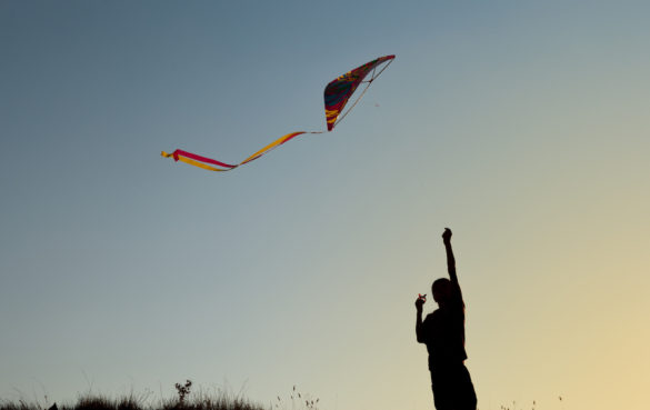 boy flies a kite in the sky at sunset with hopes of creating a new normal