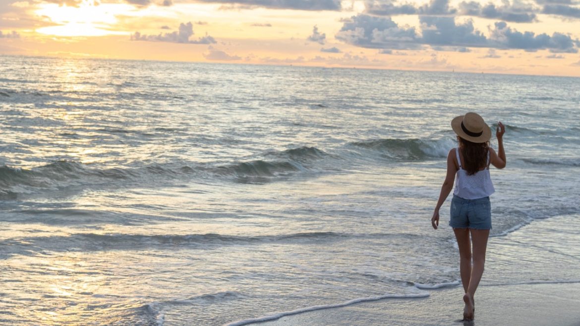 Woman takes a solo walk on beach at sunset realizing the importance of releasing negative energy