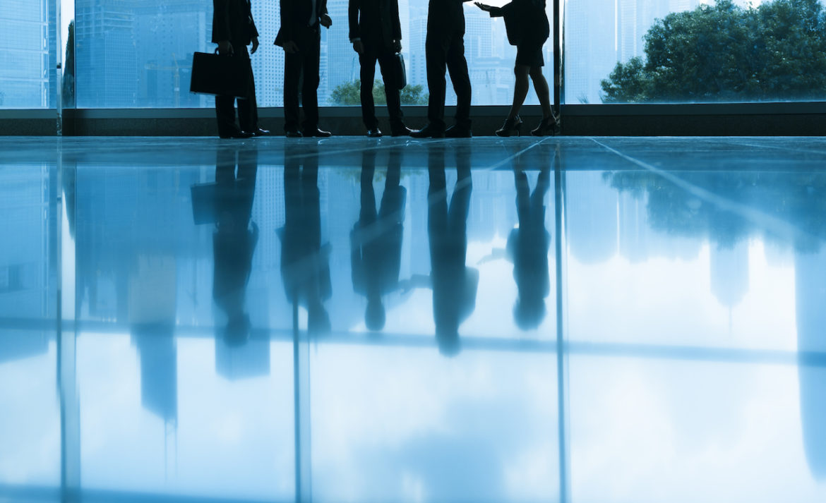 Five colleagues chance a meeting press onward with their reflections depicted upside down on the glossy tile of a high-rise building