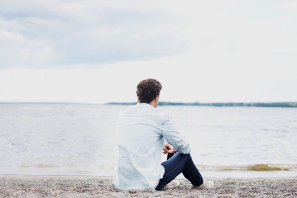 A man sitting on the pebble shoreline by the sea ponders his life and discovers it's important to follow your heart