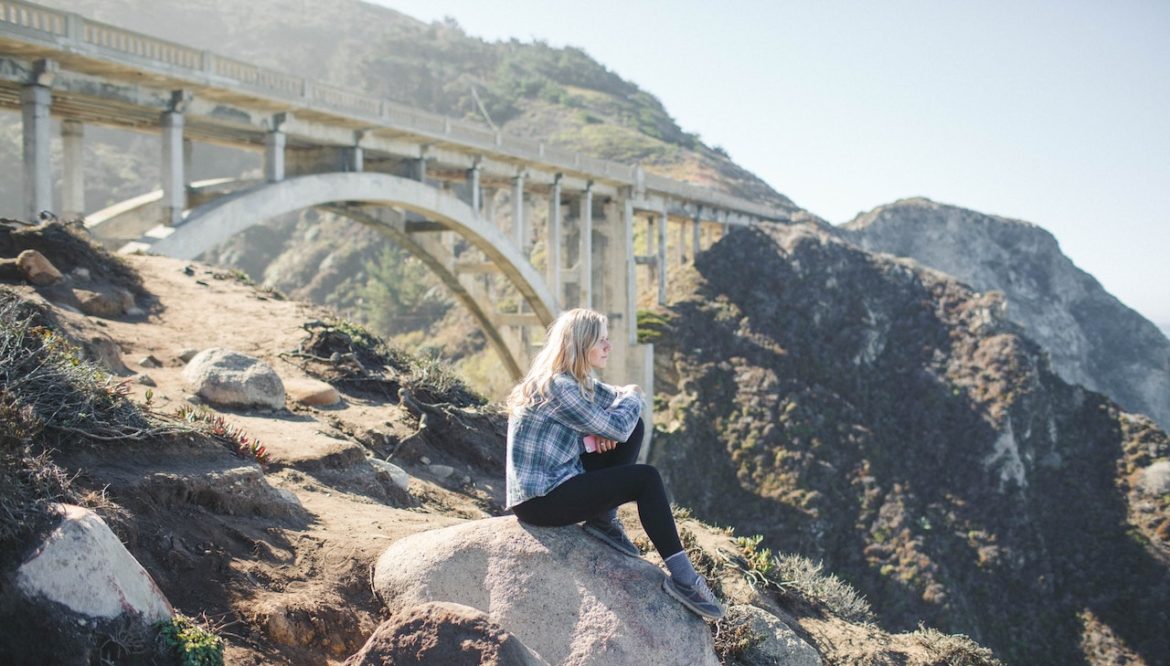 Young woman sitting on a large rock on a beautiful summer day looking out into the distance planning a whole new life