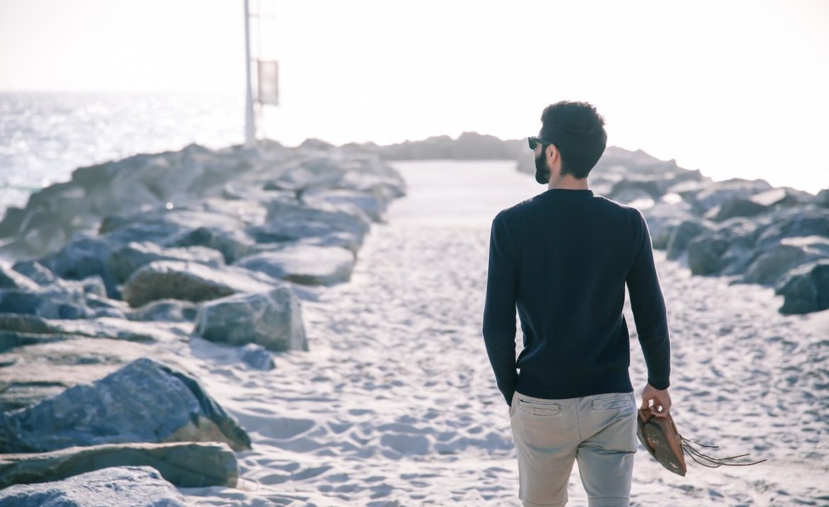 Man shifting perspective at the lake taking a leisurely walk on the sand near a rocky pier on a sunny day