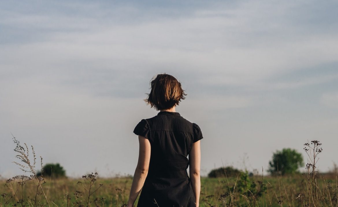 A woman stands in the meadow and finds a way to get out of a rut by enjoying nature on a beautiful summer day