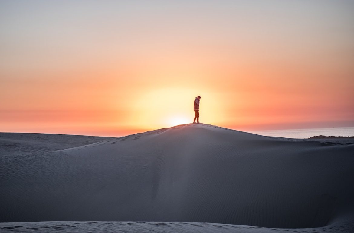A man said to himself choose you and opted for an adventure standing on top of a sand dune with the sun rising he's captured by its glow