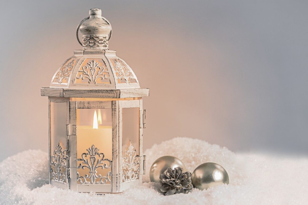 A Christmas reflection in the moment from a lit candle stationed in an ornamental lantern resting on the snow next to silver ornaments