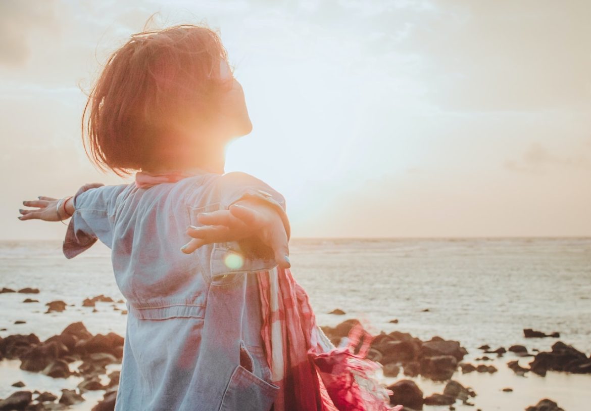 amid difficult times a woman staying optimistic standing by the sea with outstretched arms she's warmed by the sun