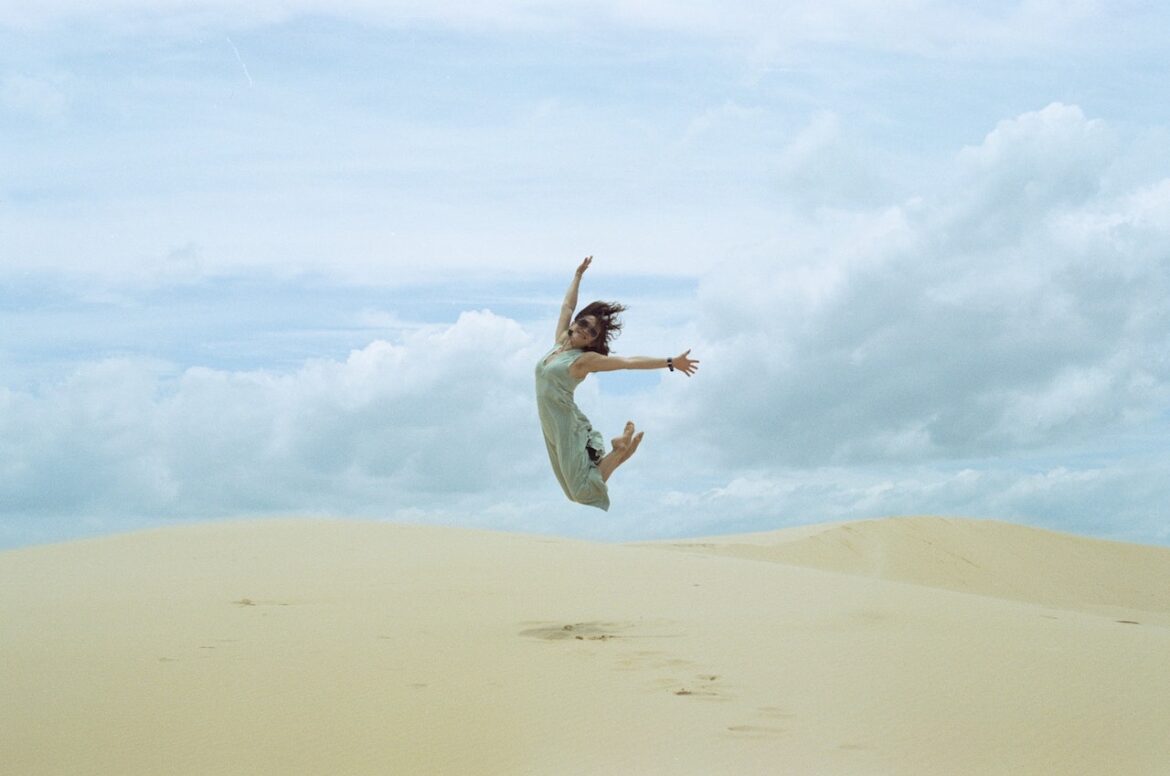 The balanced life delivers spiritual joy as woman jumps mid-air above a sand dune