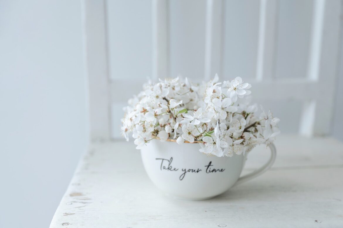 Take your time scripted on a teacup holding white flowers, sitting on a chair.