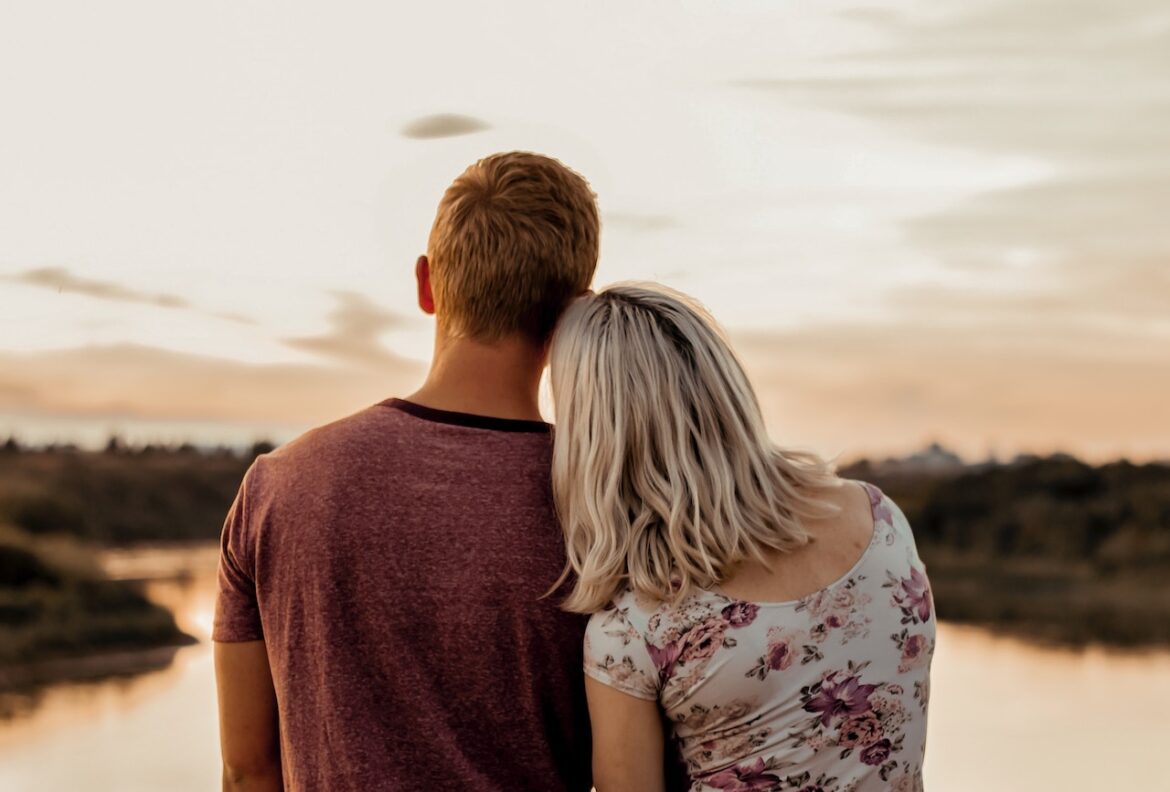 She leans on his shoulder as they face the lake at sunset, knowing he's a keeper.