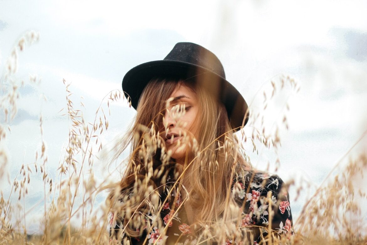 Woman standing in a wheat field wearing a vintage black hat wondering why you can't find love