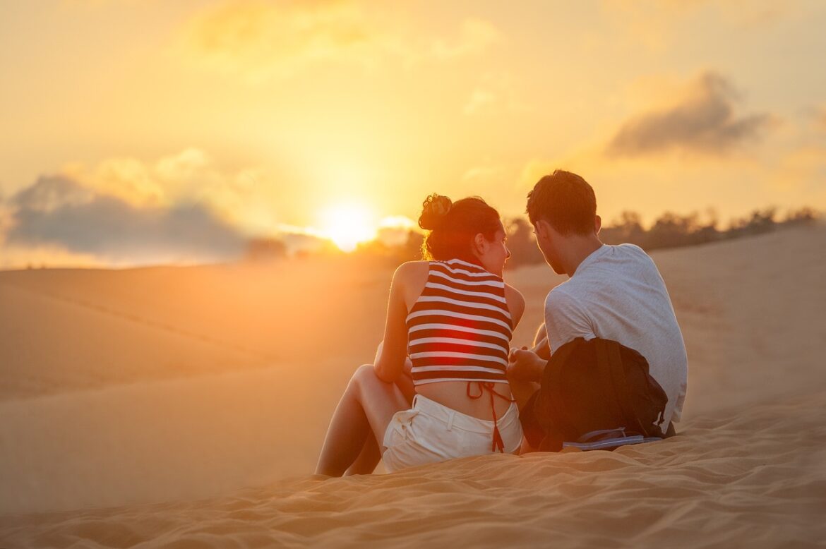 Couple at the beach sitting on the sand at sunset realizing there's a choice between high, low, or no standards when dating