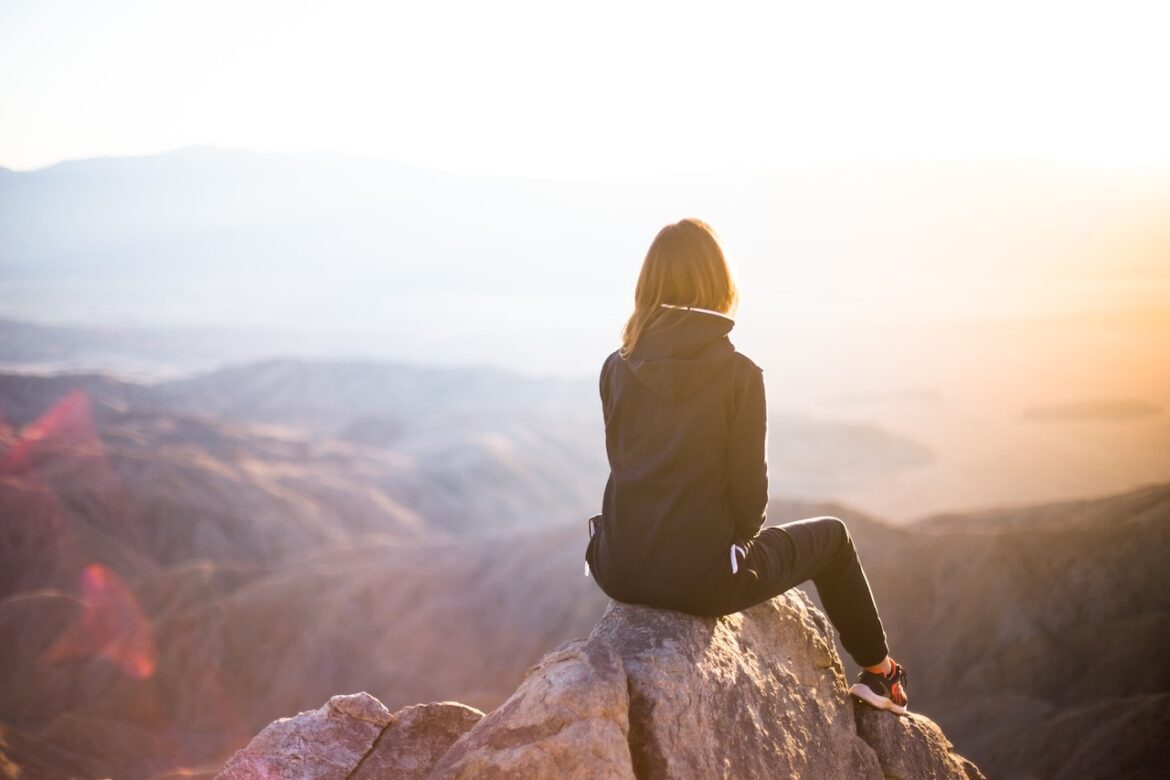 Woman seated on a rock at sunset looking out into the distance contemplating why she's dating the wrong type