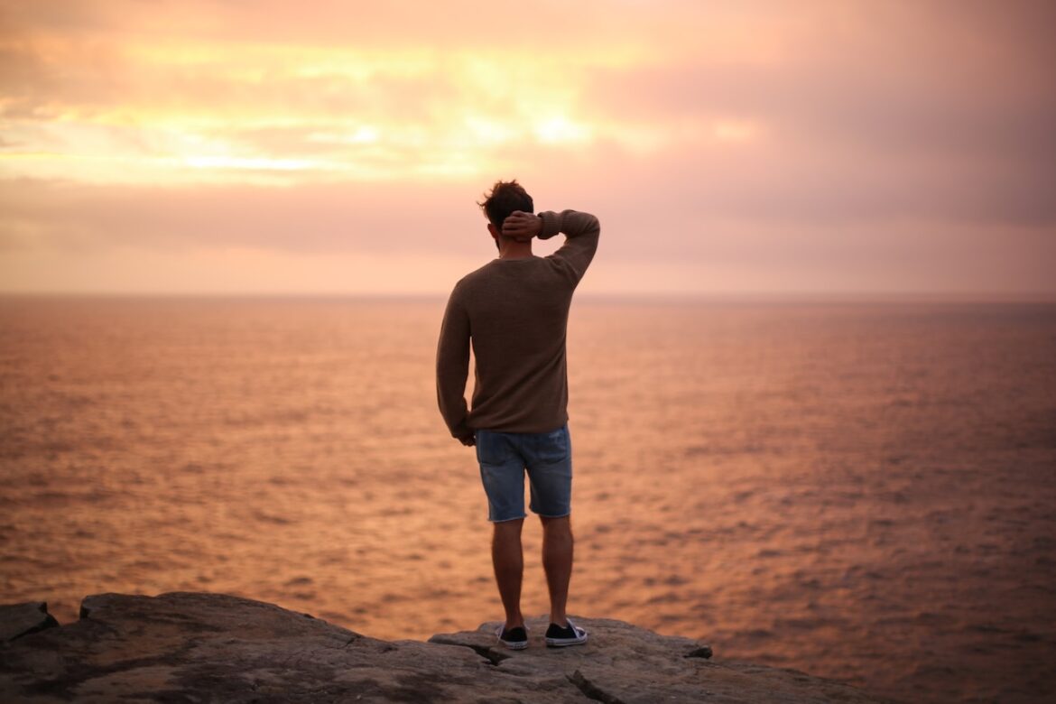 Man stands on a rock by the ocean, perplexed by his choices, as he comes to grips with that one bad decision in love.