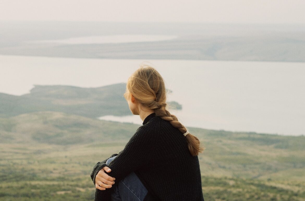 A young woman sits on a rock taking in a scenic view. She went over her thoughts only to end up questioning: why we choose what we do, in love as in life.